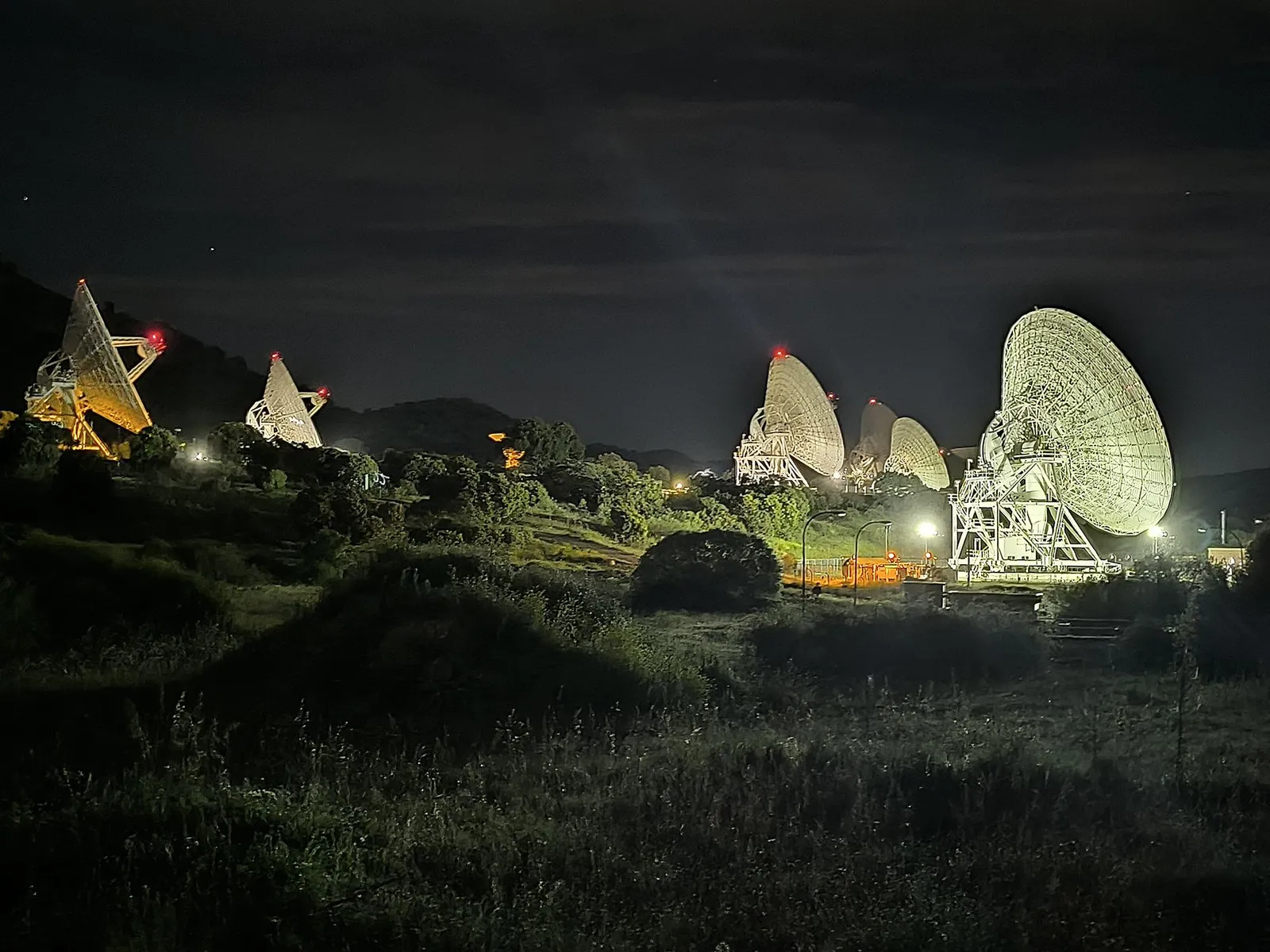 Six Deep Space Network dish antennas floodlit at night at the Madrid Deep Space Communications Complex